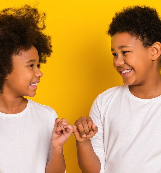 Photo of sweet friendly schoolboy schoolgirl wear white shirts holding small fingers isolated yellow color background.