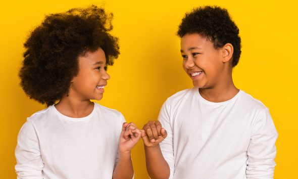 Photo of sweet friendly schoolboy schoolgirl wear white shirts holding small fingers isolated yellow color background.
