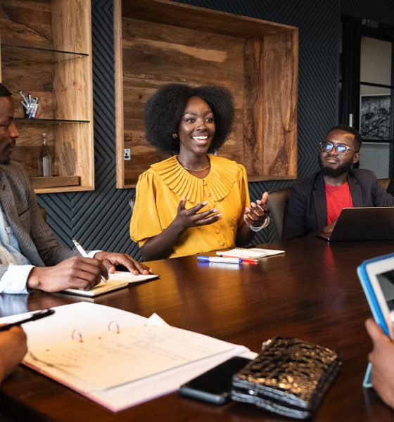 View between colleagues with focus on African professional in early 30s looking across conference table at young associate, smiling and gesturing as she speaks. (Photo by Johnny Greig)