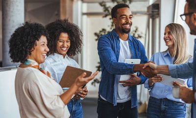 A diverse group of professionals smiling and shaking hands in a modern office environment. The image conveys teamwork, collaboration, and positive business relationships.