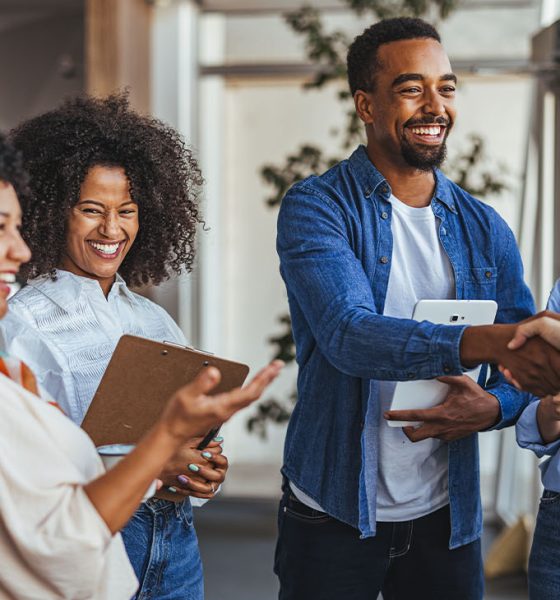 A diverse group of professionals smiling and shaking hands in a modern office environment. The image conveys teamwork, collaboration, and positive business relationships.