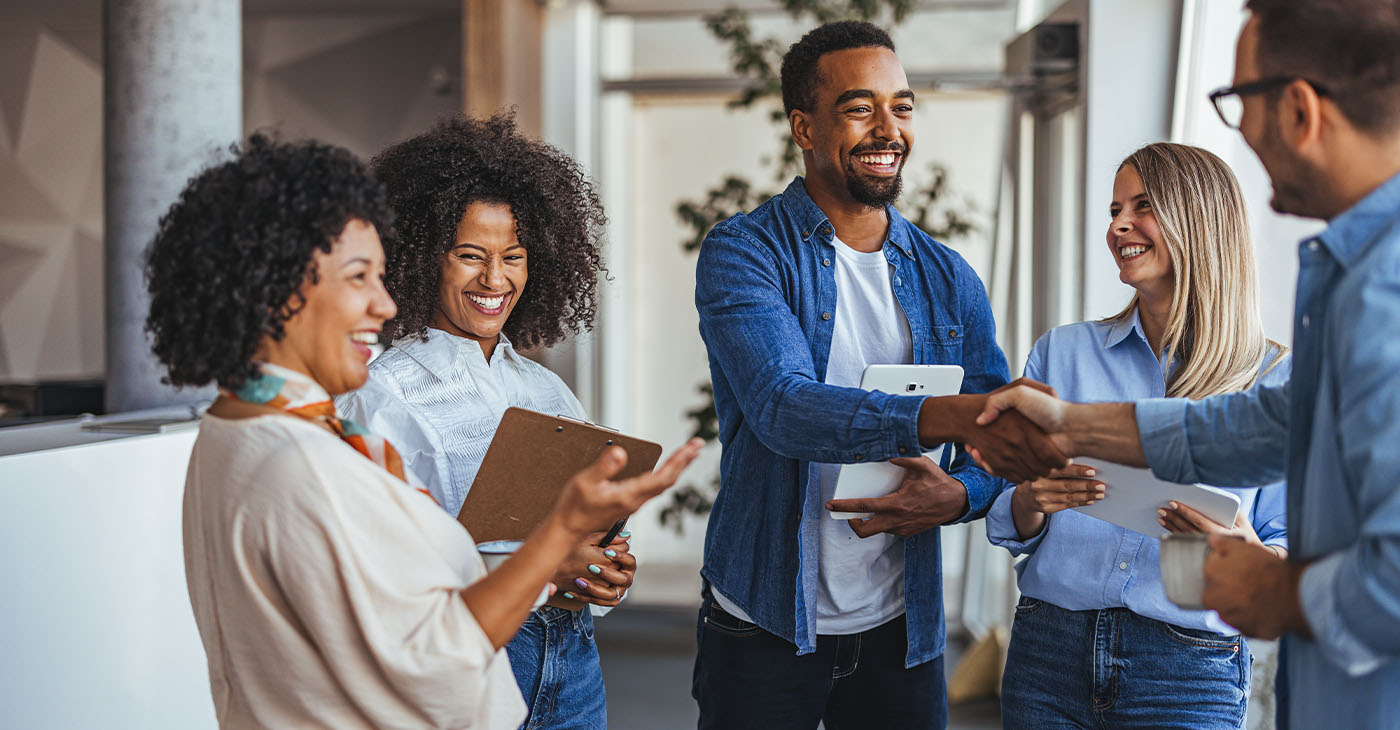 A diverse group of professionals smiling and shaking hands in a modern office environment. The image conveys teamwork, collaboration, and positive business relationships.