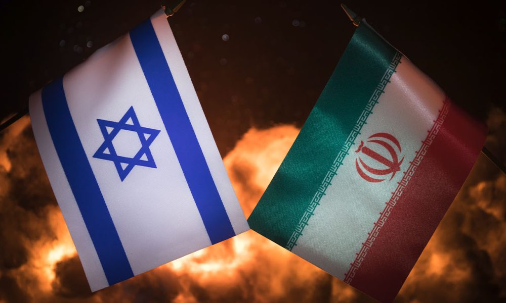 Israel and Iran small flags on burning dark background. Concept of crisis of war and political conflicts between nations. Selective focus (Photo by Zeferli)