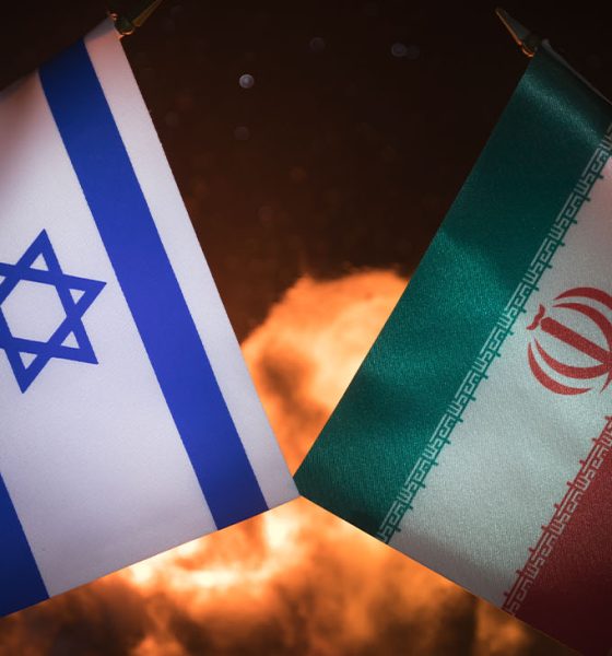Israel and Iran small flags on burning dark background. Concept of crisis of war and political conflicts between nations. Selective focus (Photo by Zeferli)