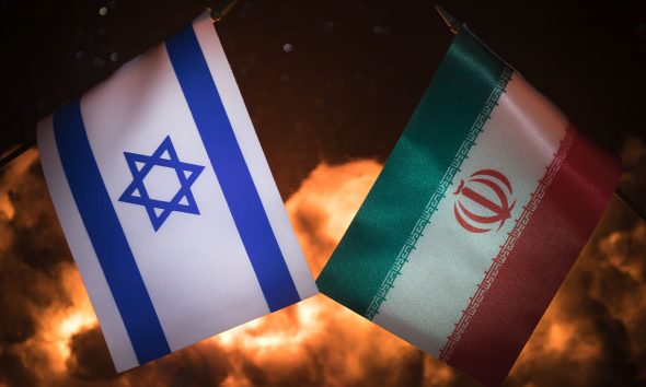 Israel and Iran small flags on burning dark background. Concept of crisis of war and political conflicts between nations. Selective focus (Photo by Zeferli)