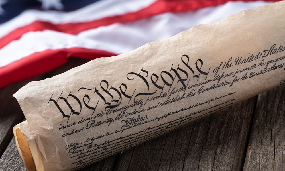United States constitution with American flag in background on rustic wooden table