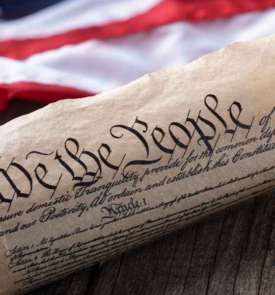 United States constitution with American flag in background on rustic wooden table