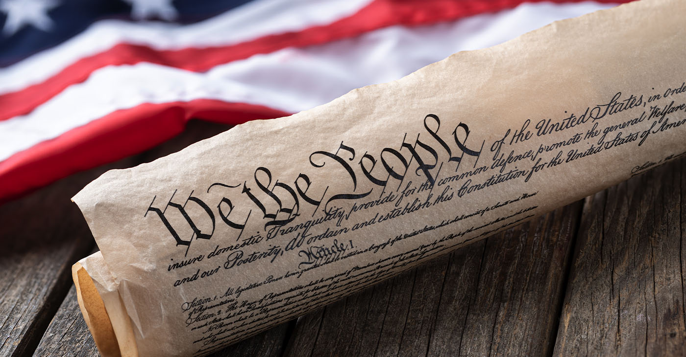 United States constitution with American flag in background on rustic wooden table