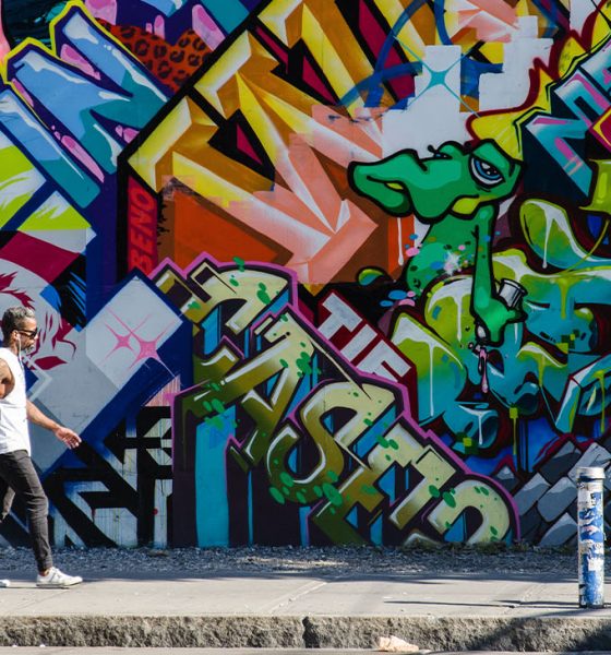 New York City, NY, USA - October 1, 2013: Hipster male walking next to a wall of graffiti in Brooklyn, New York, US.