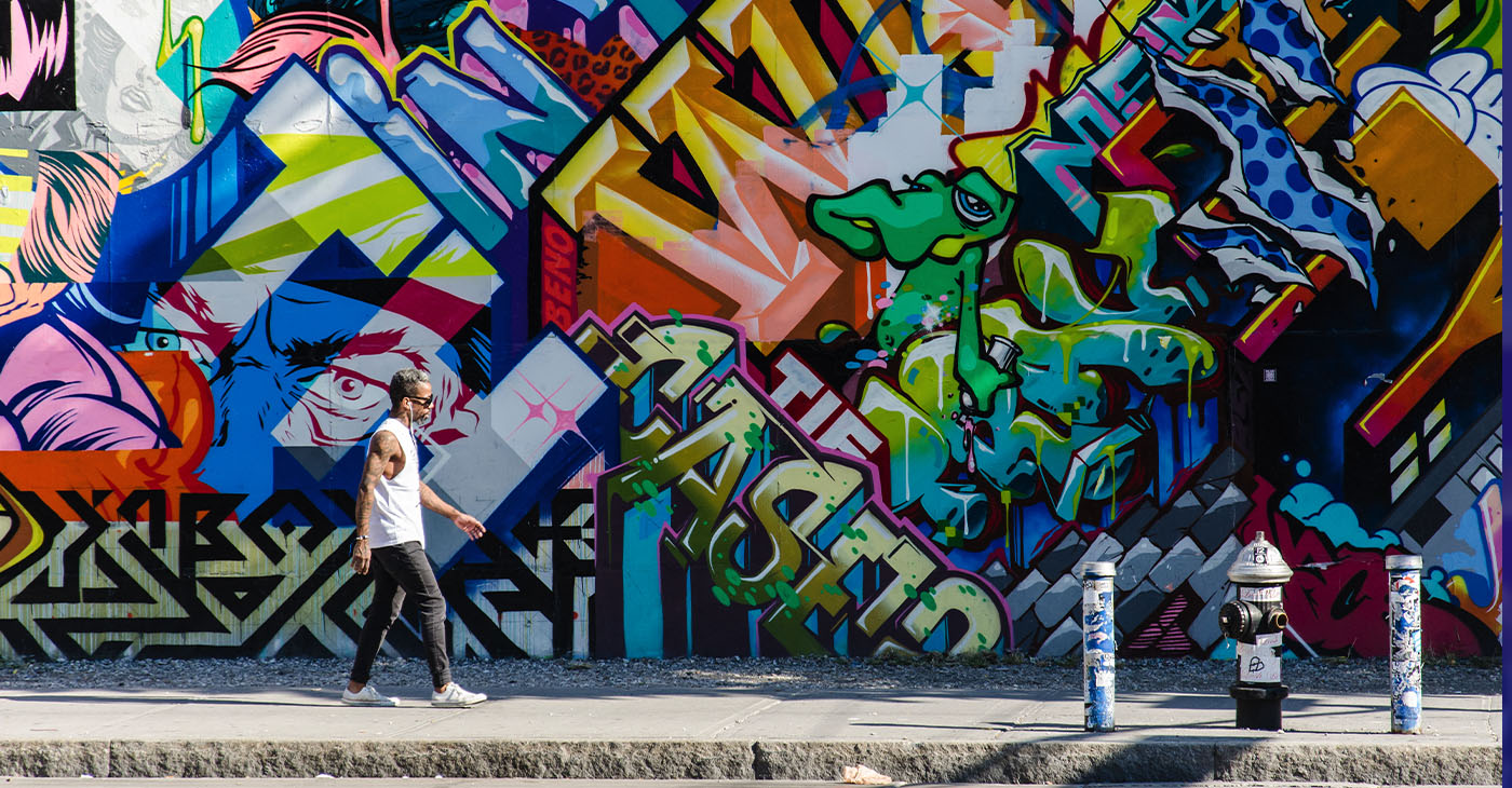 New York City, NY, USA - October 1, 2013: Hipster male walking next to a wall of graffiti in Brooklyn, New York, US.
