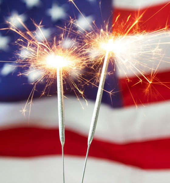 Two bright burning sparklers with an American flag in the background. 4th of July celebrations.