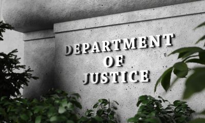 Silver sign of Department of Justice on a classical concrete wall with plants as foreground. Illustration of the concept of enforcement of federal laws