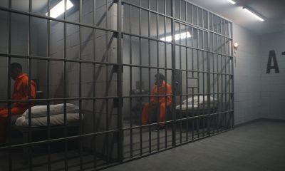 African American inmates in detention center or correctional facility. Depressed man in orange uniform sits on prison bed and looks at barred window. Prisoners serve imprisonment term in jail cell.
