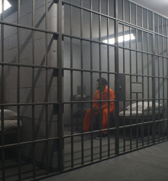 African American inmates in detention center or correctional facility. Depressed man in orange uniform sits on prison bed and looks at barred window. Prisoners serve imprisonment term in jail cell.