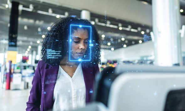 Focused young businesswoman standing at an airport check-in kiosk, with facial recognition technology digitally scanning her face, highlighting advanced security, innovation, and efficiency in modern travel.Focused young businesswoman standing at an airport check-in kiosk, with facial recognition technology digitally scanning her face, highlighting advanced security, innovation, and efficiency in modern travel.