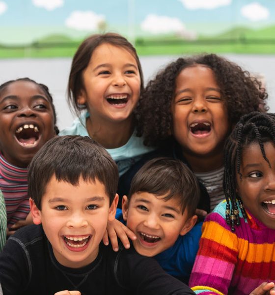 A group of diverse kids smile in this portrait. They are stacked on top of each other while cuddling in close and showing how happy they are.