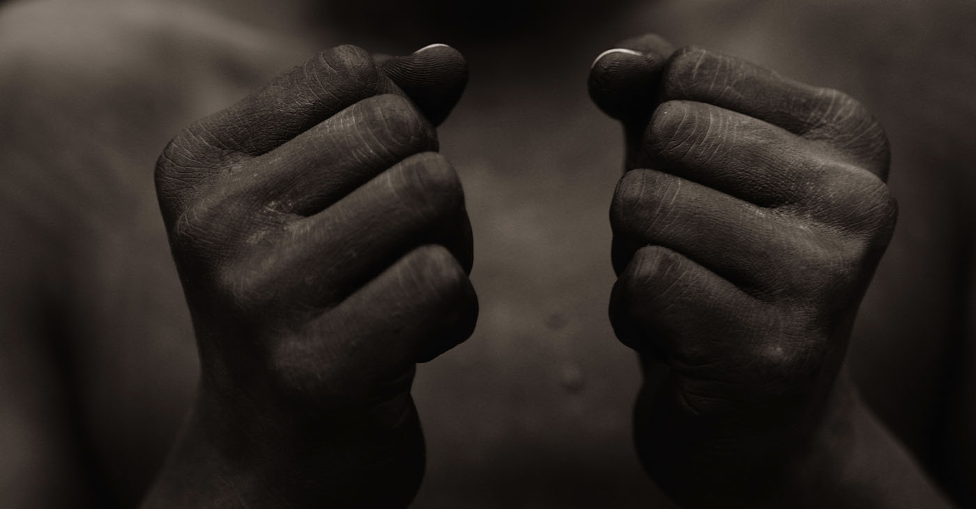 Black person with wearing black paint, holding fist in front of chest in sign of freedom and power.