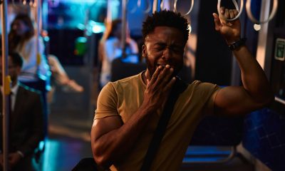 Sleepy young man covers his mouth while yawning and holding onto the railing of a night bus, other passengers are visible in the background (Photo by Igor Suka)