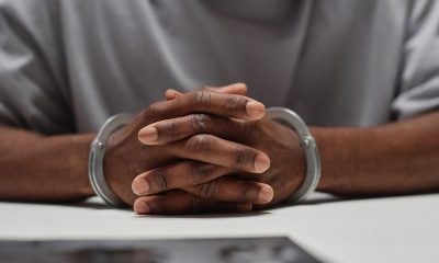 Close up of anonymous black man wearing handcuffs sitting at table in police department with hands clasped, copy space