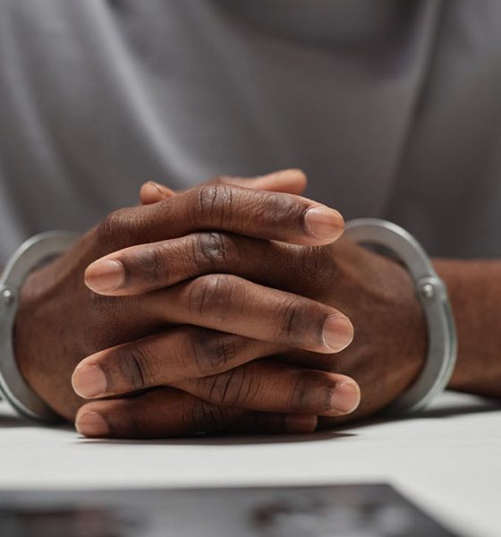 Close up of anonymous black man wearing handcuffs sitting at table in police department with hands clasped, copy space