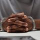 Close up of anonymous black man wearing handcuffs sitting at table in police department with hands clasped, copy space
