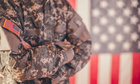 Man, dressed in USA army uniform, posing in front of an American flag