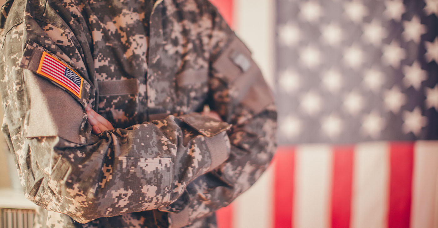 Man, dressed in USA army uniform, posing in front of an American flag