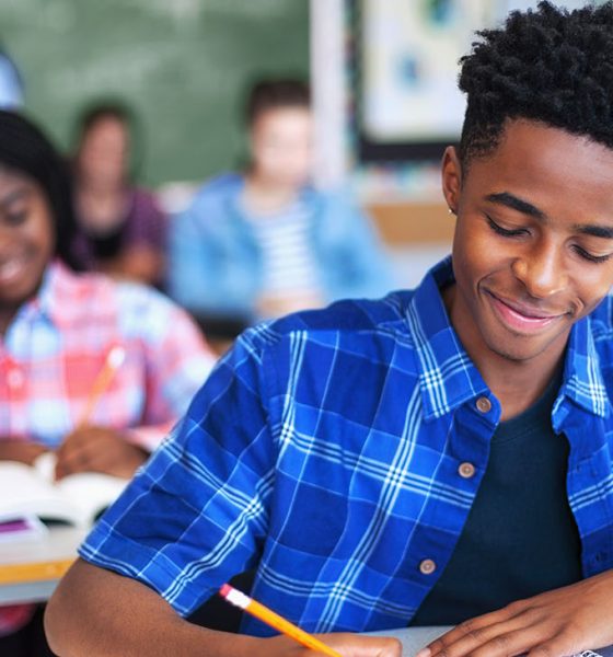 Smiling male student writing in classroom. Teenage boy is concentrating at high school. He is sitting at desk.