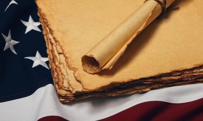 Close up blank old vintage yellow paper sheets and scroll on cotton embroidered US national flag background, symbol of American history, elevated high angle view