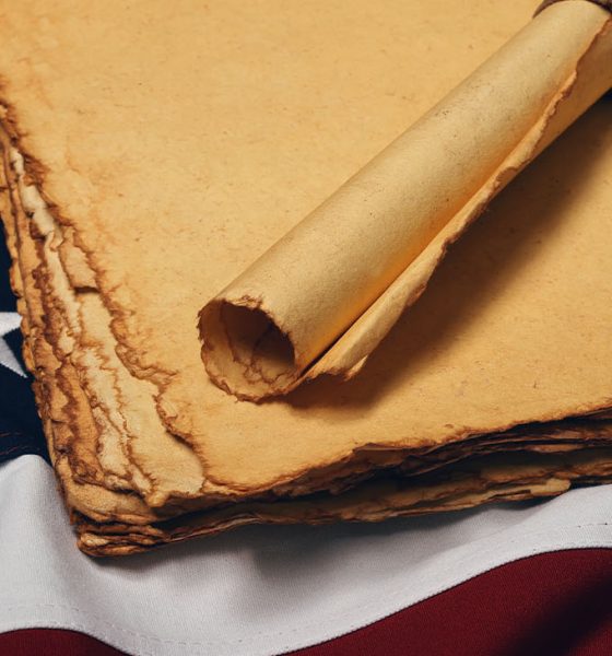 Close up blank old vintage yellow paper sheets and scroll on cotton embroidered US national flag background, symbol of American history, elevated high angle view