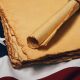 Close up blank old vintage yellow paper sheets and scroll on cotton embroidered US national flag background, symbol of American history, elevated high angle view