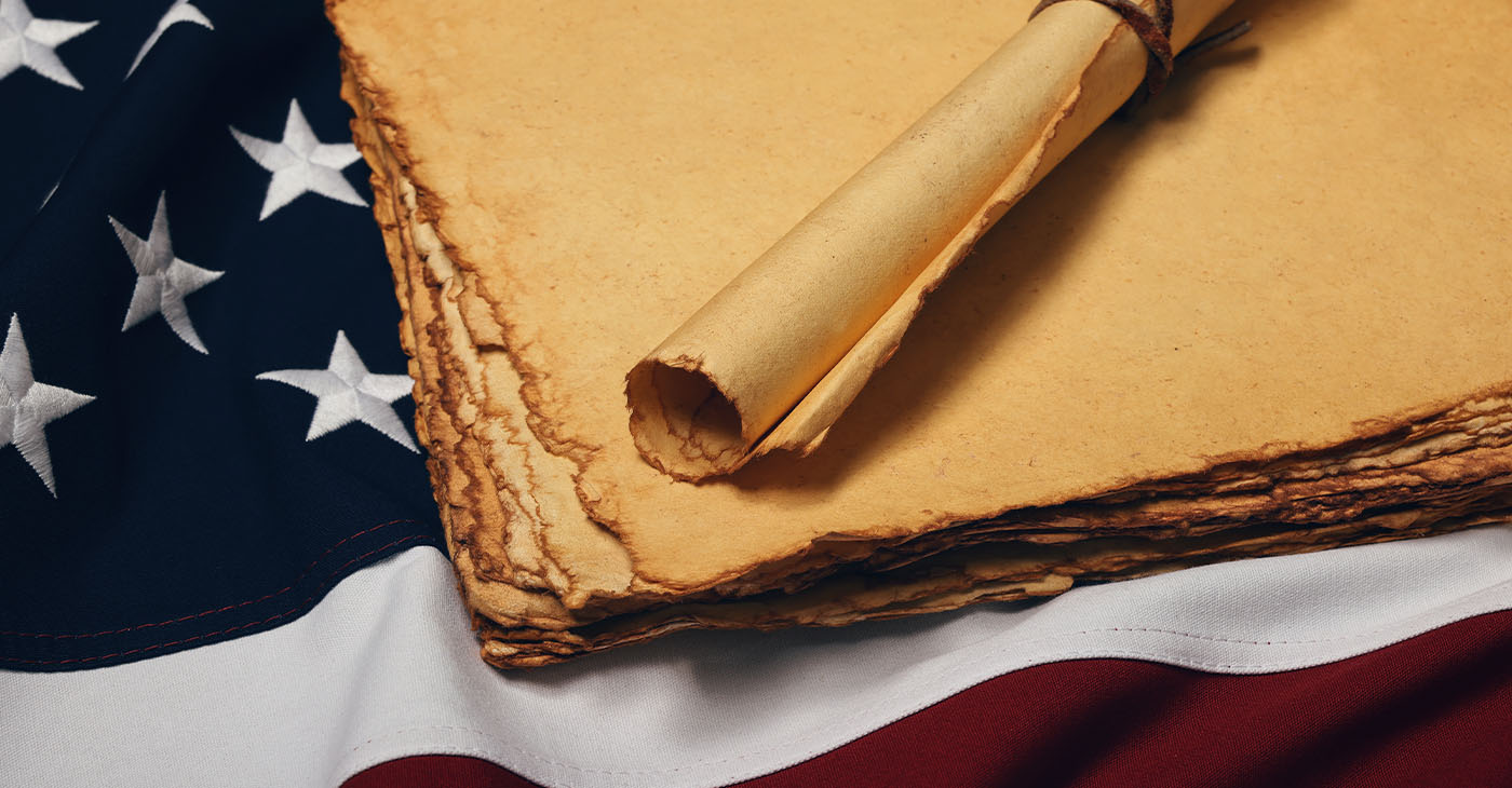 Close up blank old vintage yellow paper sheets and scroll on cotton embroidered US national flag background, symbol of American history, elevated high angle view