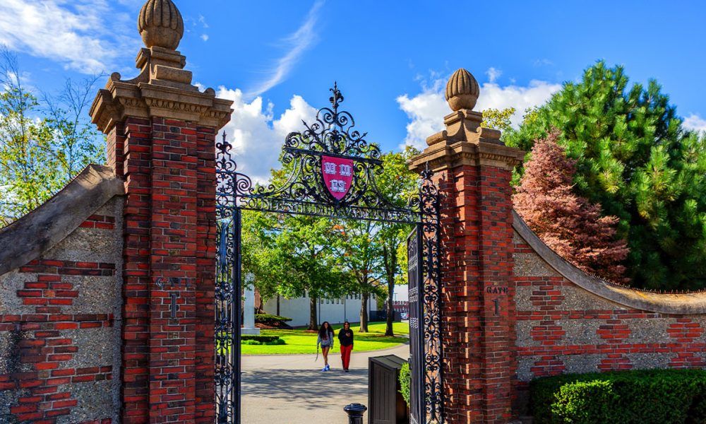 Boston, Massachusetts, USA - October 9, 2023: Gate 1, the Newell Gate pedestrian entrance to Harvard University's Soldiers Field Athletic Area. Atop the gate is the Harvard crest, logo, with three books and the word VERITAS (Truth). Two student pedestrians.