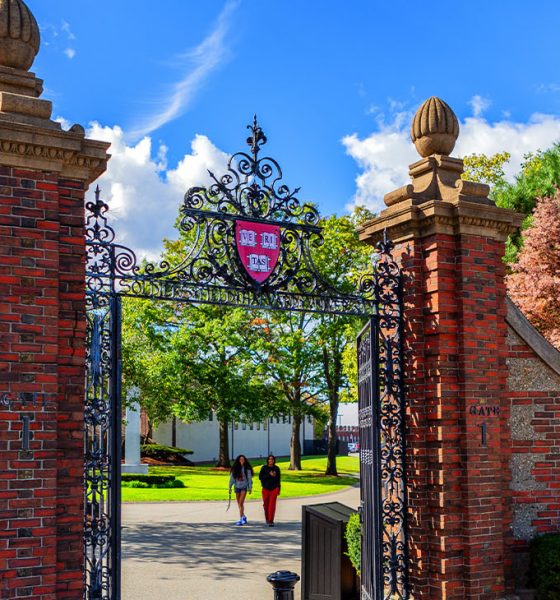 Boston, Massachusetts, USA - October 9, 2023: Gate 1, the Newell Gate pedestrian entrance to Harvard University's Soldiers Field Athletic Area. Atop the gate is the Harvard crest, logo, with three books and the word VERITAS (Truth). Two student pedestrians.