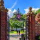 Boston, Massachusetts, USA - October 9, 2023: Gate 1, the Newell Gate pedestrian entrance to Harvard University's Soldiers Field Athletic Area. Atop the gate is the Harvard crest, logo, with three books and the word VERITAS (Truth). Two student pedestrians.