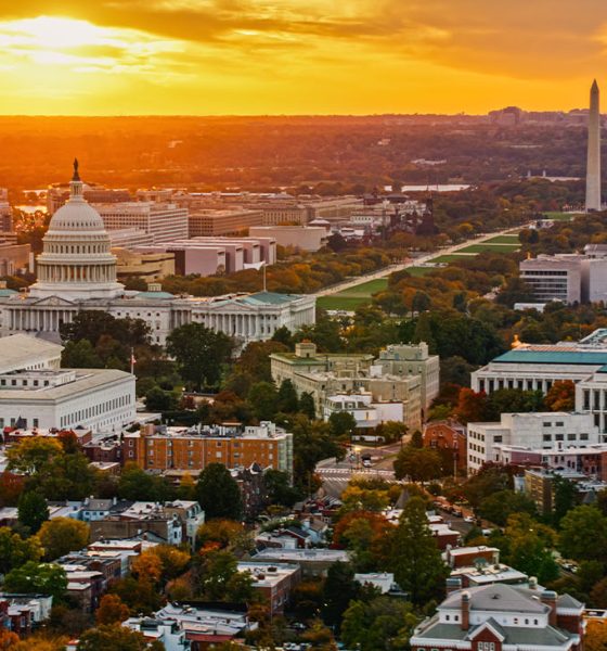 Helicopter shot of Capitol Hill in Washington, D.C. at sunset on a fall evening, looking over residential streets towards the U.S. Capitol Building, Supreme Court, and the National Mall.