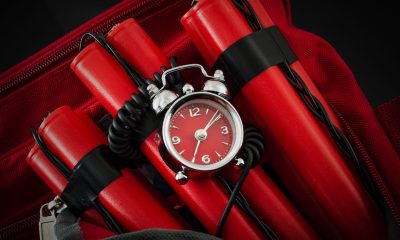 Terrorism and bomb threat concept with dynamite or TNT stick, alarm clock, black wires and a red duffle bag with dark dramatic lighting