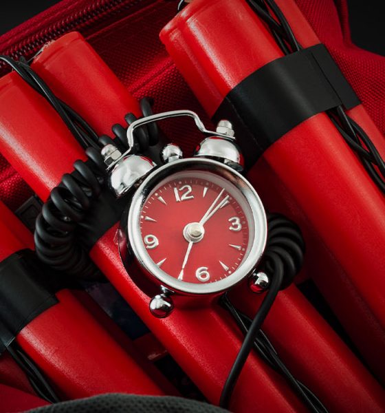 Terrorism and bomb threat concept with dynamite or TNT stick, alarm clock, black wires and a red duffle bag with dark dramatic lighting