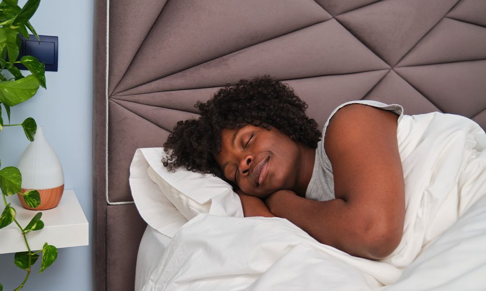 Happy young woman sleeping on white sheets in bed in a room with a plant. Resting asleep.