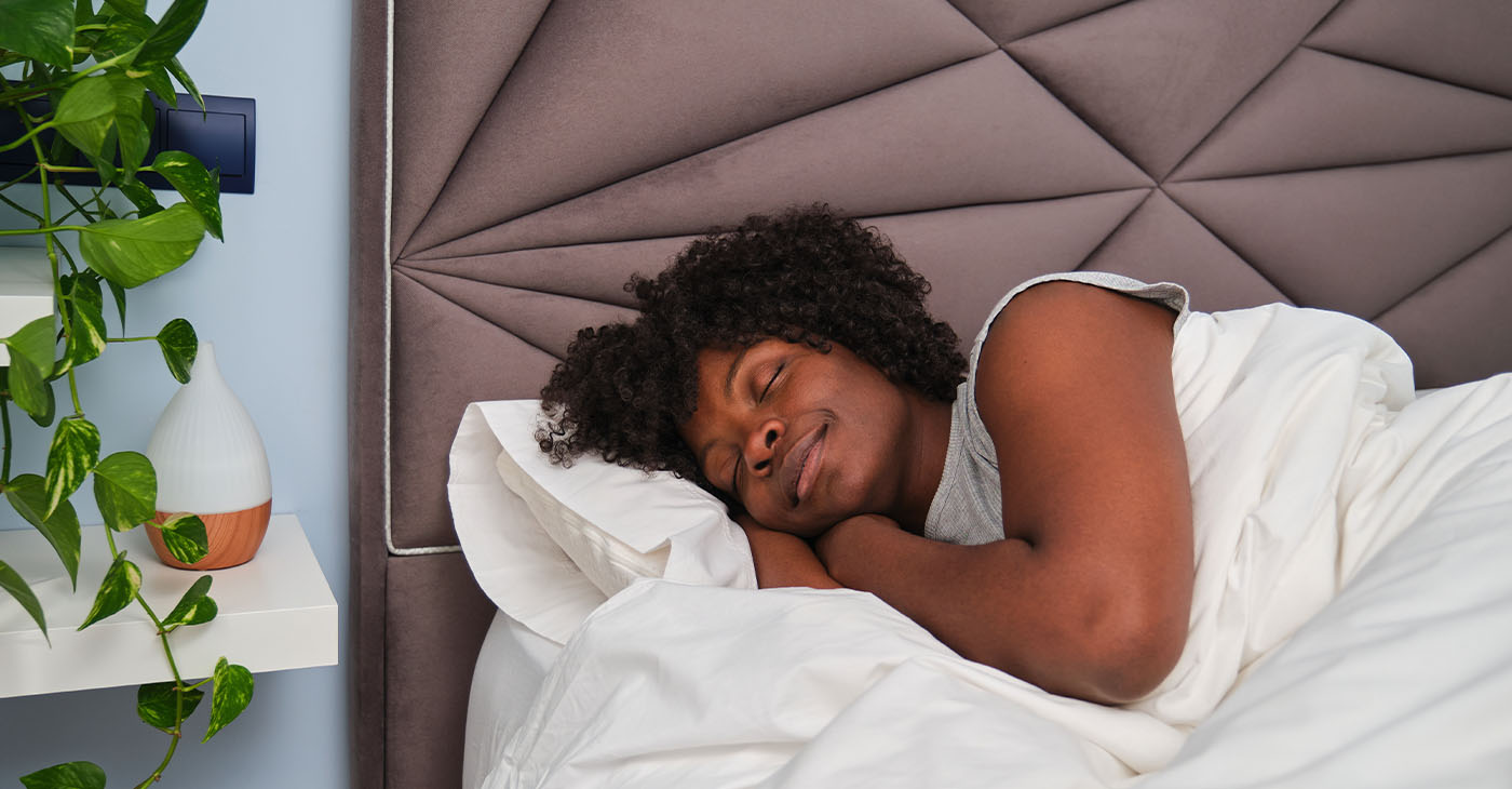 Happy young woman sleeping on white sheets in bed in a room with a plant. Resting asleep.