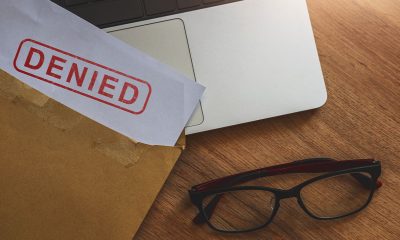 Document with denied stamp put on the laptop on wooden table