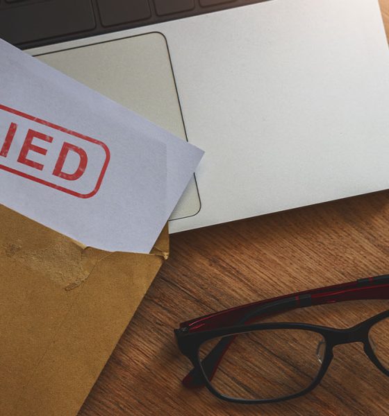 Document with denied stamp put on the laptop on wooden table