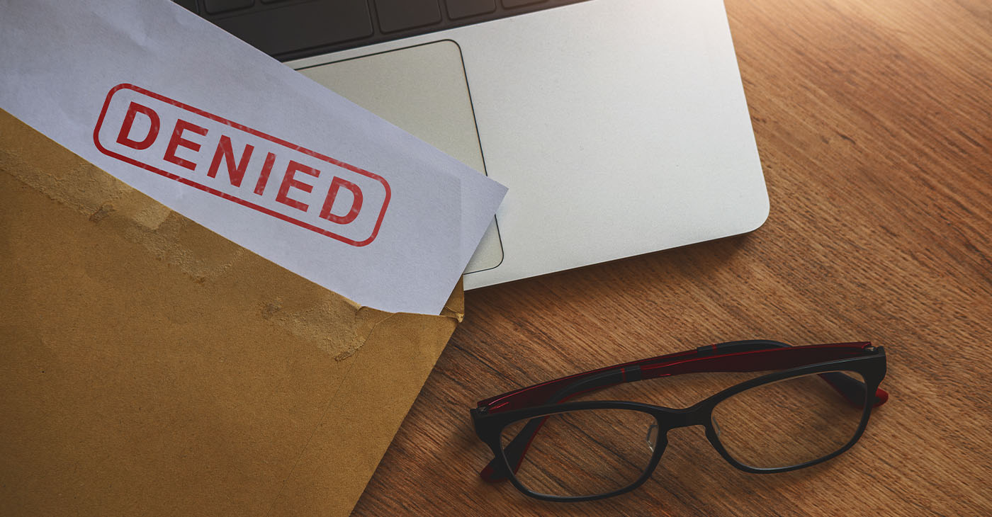 Document with denied stamp put on the laptop on wooden table