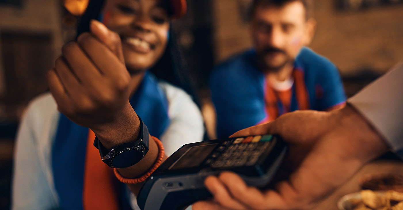 Close up of a woman paying contactless with smart watch during sports championship in a bar. (Photo by Drazen Zigic)