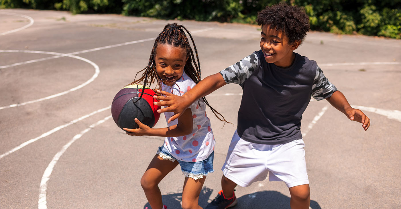 Brother and sister playing basketball and having fun outdoors.