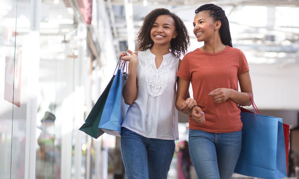 Closeup portrait of two smiling black pretty girls carrying bags, chatting and walking in shopping mall