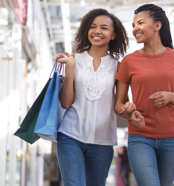 Closeup portrait of two smiling black pretty girls carrying bags, chatting and walking in shopping mall