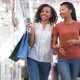 Closeup portrait of two smiling black pretty girls carrying bags, chatting and walking in shopping mall