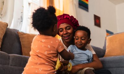 Happy mother spending quality time with her adorable baby daughter and son, playing together on the floor in their cozy living room