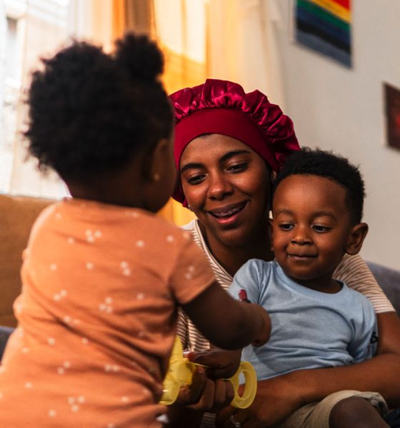 Happy mother spending quality time with her adorable baby daughter and son, playing together on the floor in their cozy living room